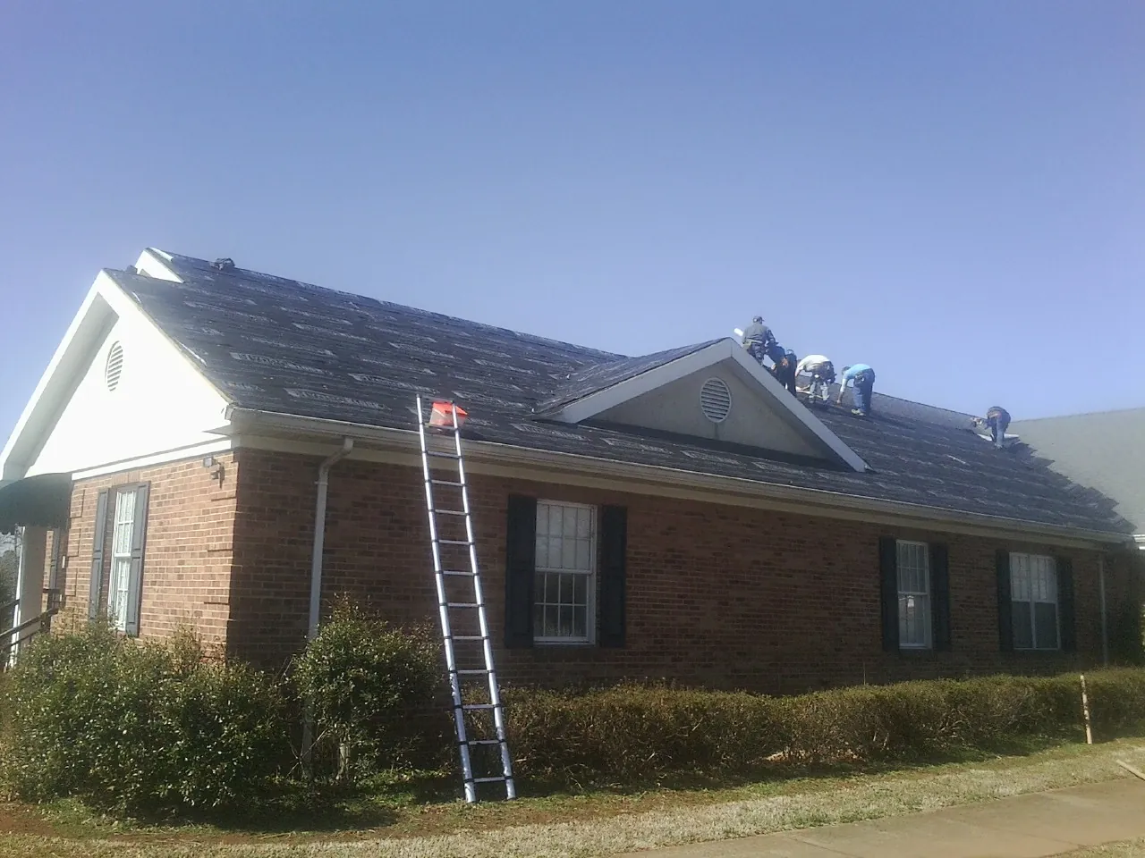 Crew tearing shingles off a brick ranch roof with a ladder set — Metal Roof Repair work by our crew in Mechanicsville