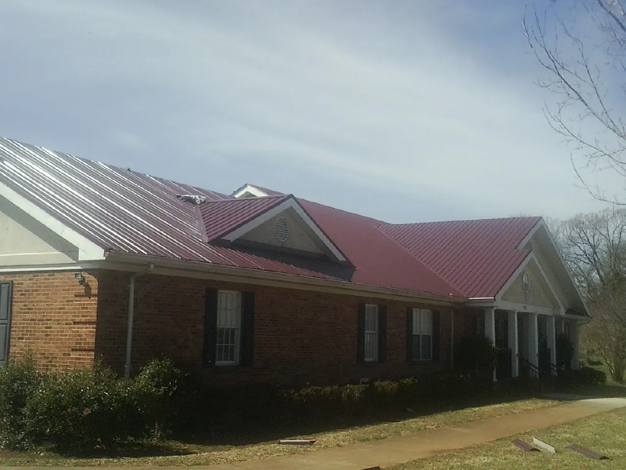 Red metal roof with gabled entries on a long brick building, from a Hail Damage Roof Repair job in Mechanicsville