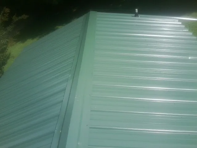 New green metal panels meeting at the ridge of a roof — Flat Roof Repair work by our crew in Mechanicsville