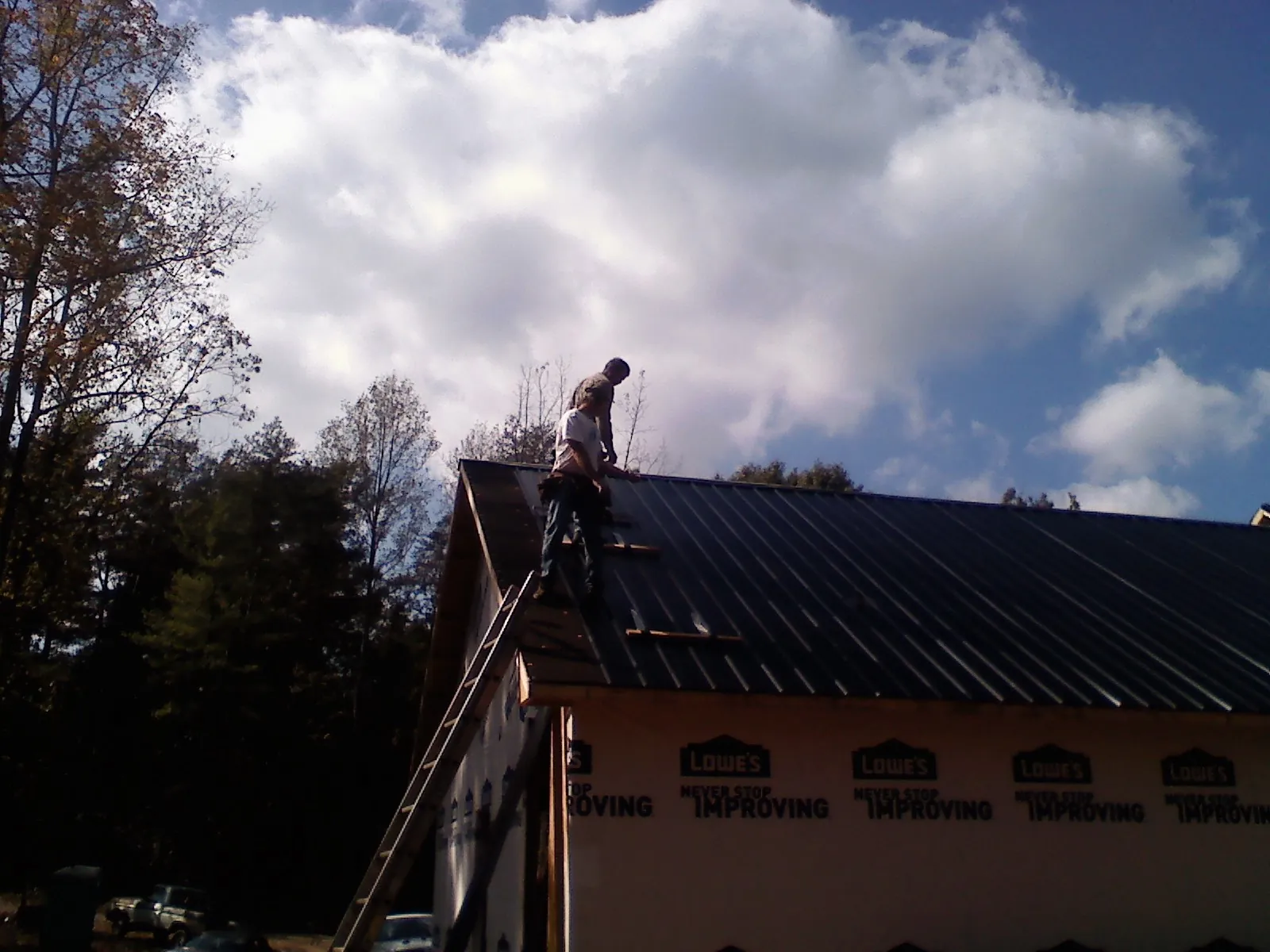 Roofer fastening dark metal panels high against a cloudy sky, from a Roof Inspection job in Mechanicsville