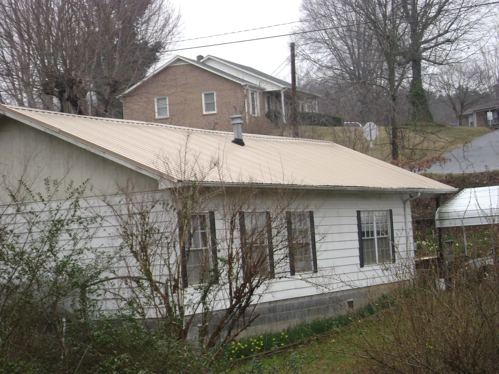 Tan metal roof on a white sided house set into a hillside — Commercial Roofing by Roofing Brothers in Mechanicsville