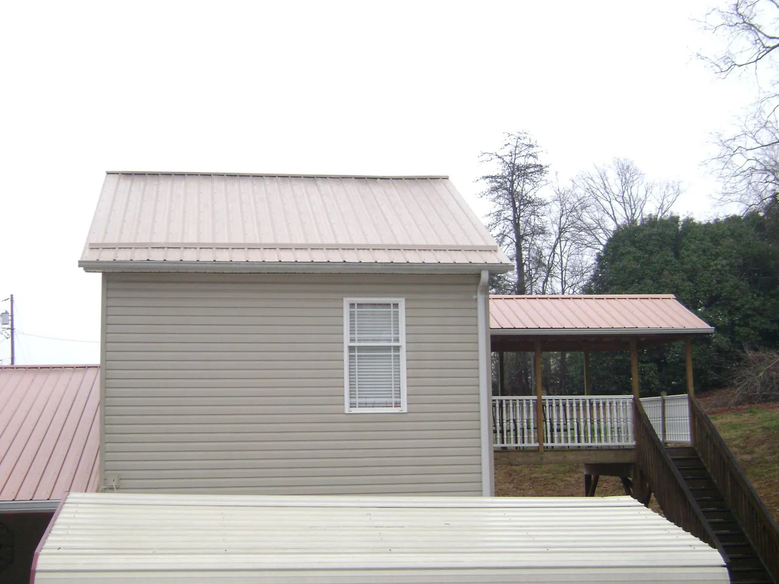 Tan metal roofs on a two story addition and attached porch, from a Roof Replacement job in Mechanicsville